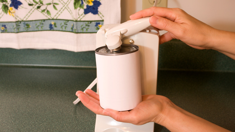 A person opens a can using a vintage electric can opener.