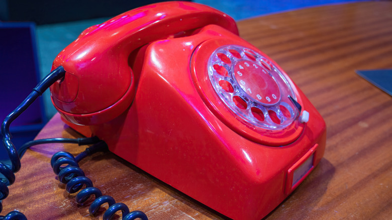 A red rotary phone with a black cord sits on a wooden desk.