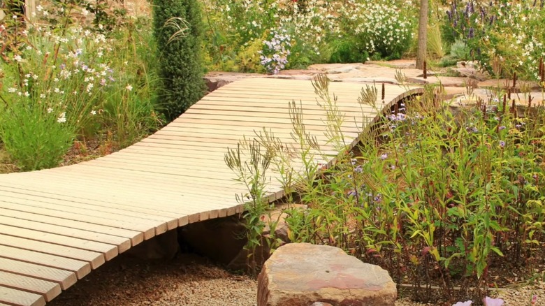 a raised wooden pathway through a garden made from wooden stakes