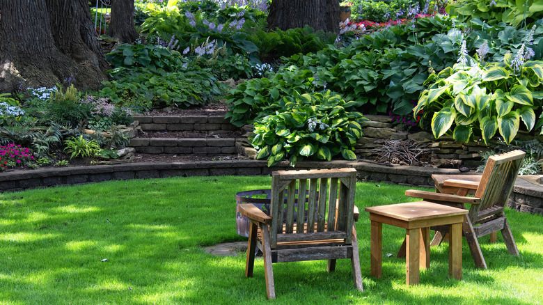 a terraced garden surrounds an entertainment area with chairs, a table, and a fire pit