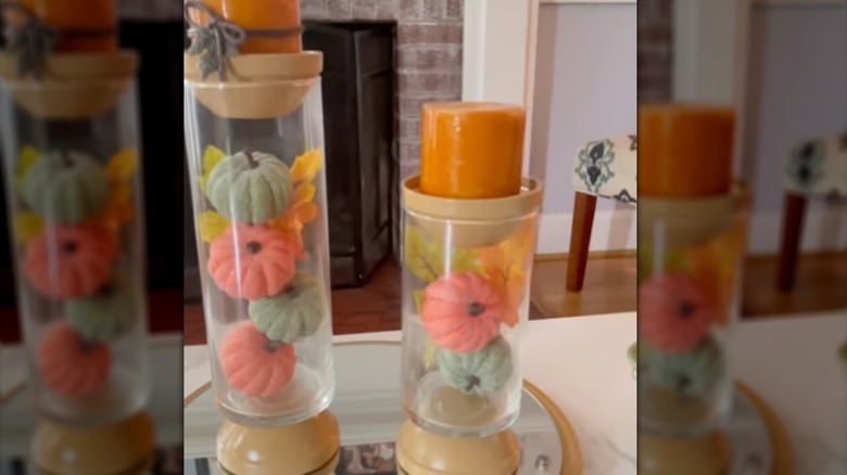 Hurricane vase filled with pumpkins and leaf motifs with a candle on top