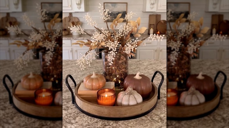 Small pine cones filling a vase with flowers and set on a wood tray in a kitchen