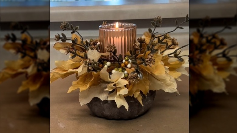 Brown pumpkin holding florals and an LED candle in a ribbed vase