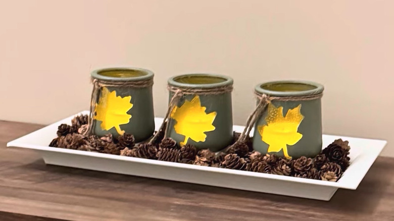 White tray filled with mini acorns features three green candle jars with a leaf silhouette on the front