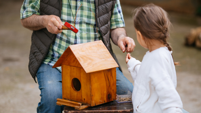 a grandfather and young girl building a bird house with a large entry hole