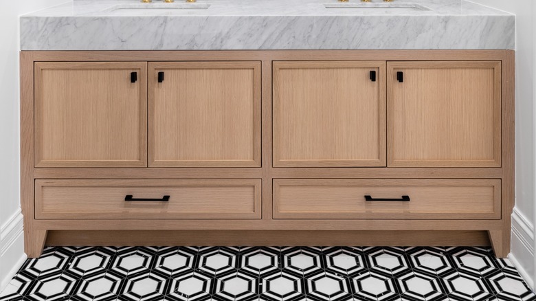 A white oak bathroom vanity with marble countertop and geometric tile flooring.