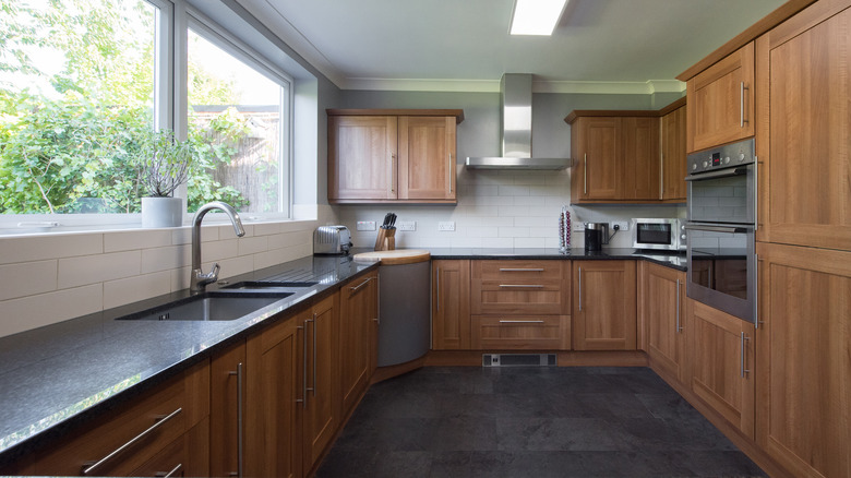 A kitchen with white oak cabinets, dark granite countertops, and a dark tile floor.