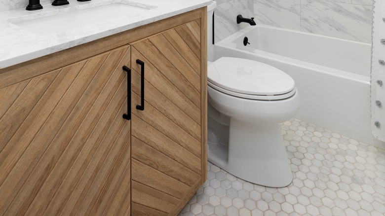 A close up of a bathroom vanity, toilet, tub, and geometric tile flooring.