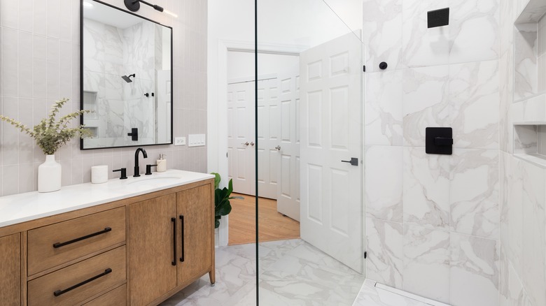 An angled photo of a bathroom with a walk-in shower, white oak vanity, and marble flooring and wall tile.