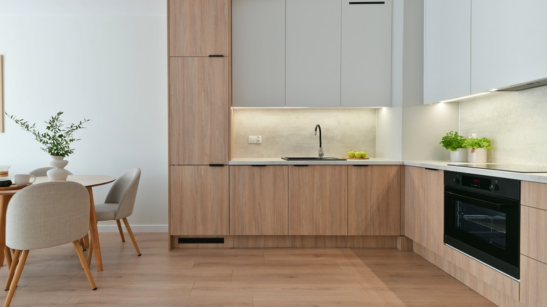 A modern kitchen with white upper cabinets and a sleek white oak lower cabinets and matching white oak floors.