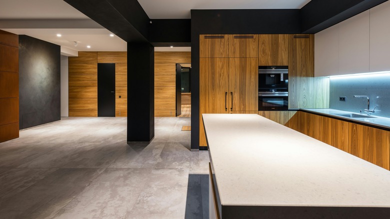 An open-concept, contemporary living room and kitchen design with wooden cabinets and walls with concrete floors.