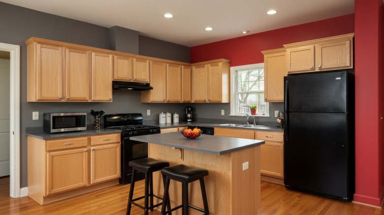 A kitchen with traditional white oak cabinets, red oak floors, and red and gray accent walls.