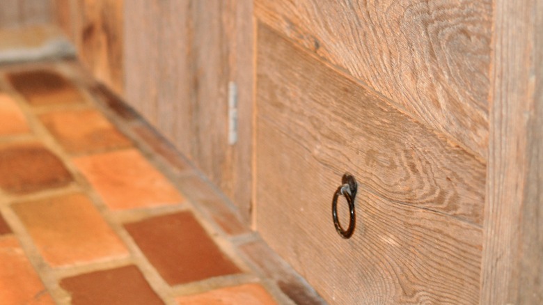 A close up image of terra cotta tile floors with vintage white oak cabinets and round drawer pulls.