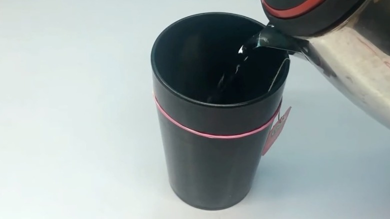 Pouring hot water into black cup with tea bag