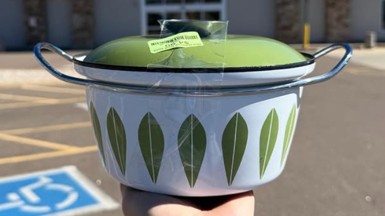 A hand holds up a vintage green and white lidded pot in front of a thrift store