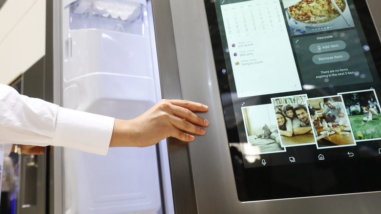 Hand opening door of smart fridge with large screen