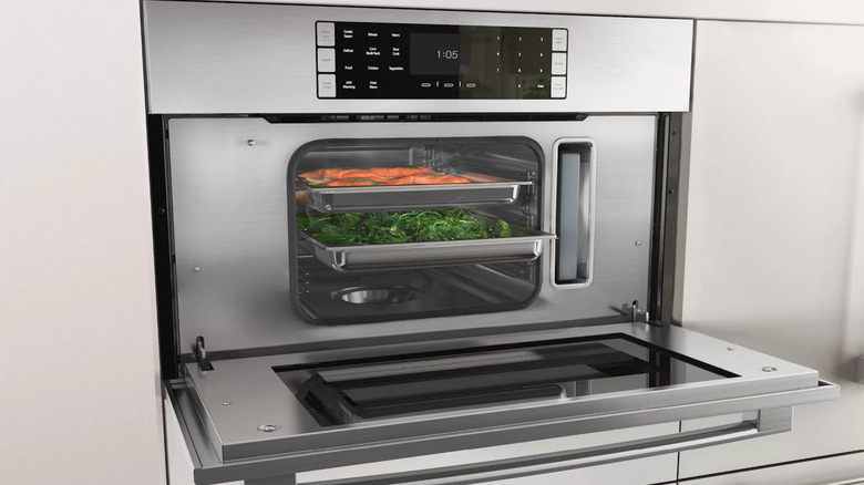 close up of a stainless steel steam oven filled with veggies on trays