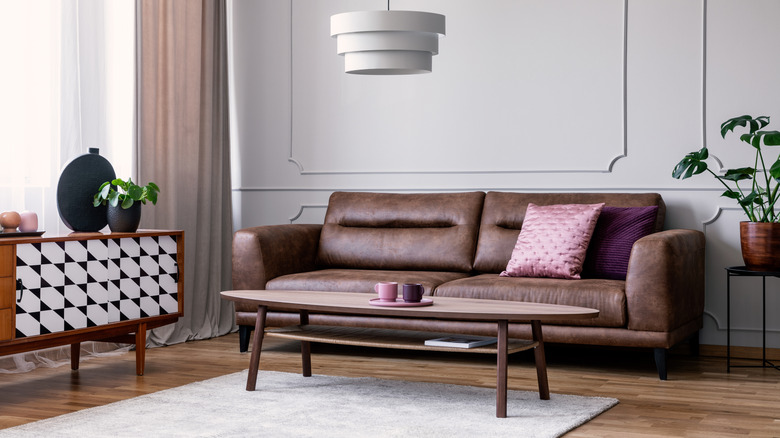 A chocolate-brown sofa with purple and pink pillows and an oval coffee table