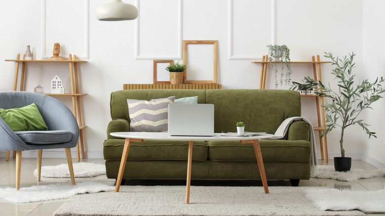 An olive two-seat sofa in a living room with a blue accent chair and bookshelves in light finishes