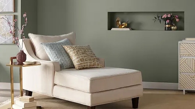 A cream chaise lounge in front of a muted green wall.