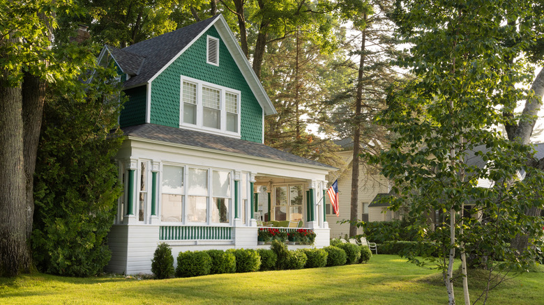 Green and white house with a front porch surrounded by mature trees
