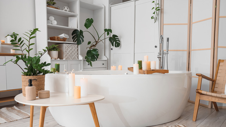 A bathroom featuring a stand alone tub flanked by various plants and candles.