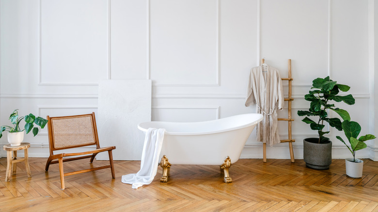 A bathroom with a chair and plants next to the tub.