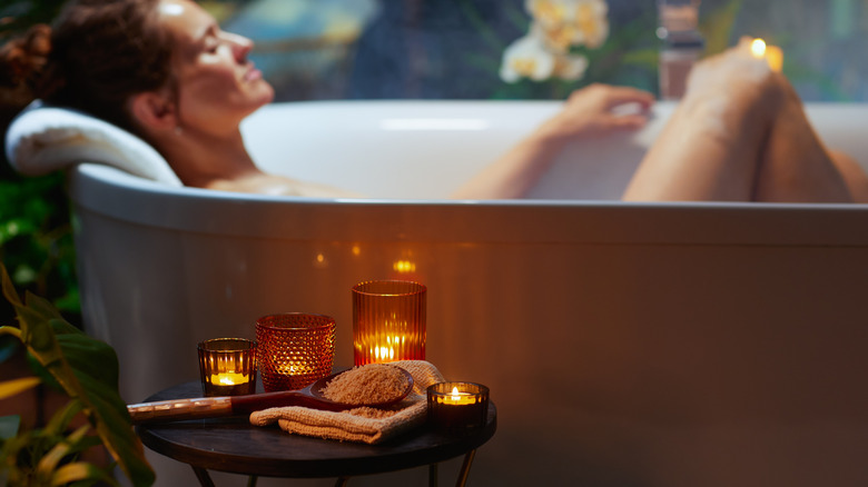 A blurred woman taking a bath in the background with candles and bath salts in the foreground.