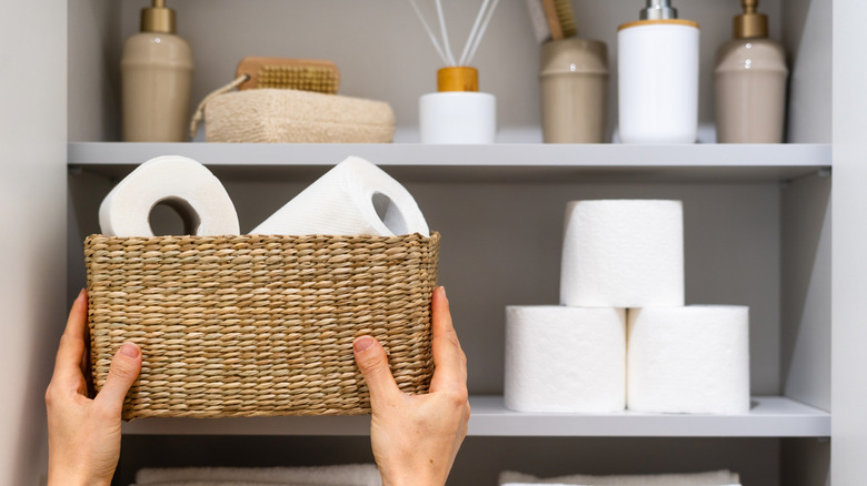 Hands placing a basket full of toilet paper next to a neat pile of toilet paper rolls.