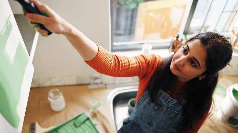 Woman painting a white cabinet green