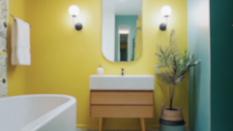Yellow bathroom with a tub and a plant in a wood stand
