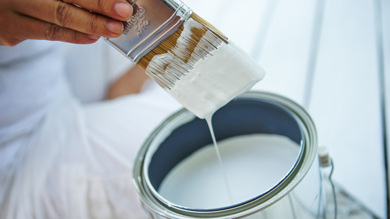 A hand dipping a brush in white paint