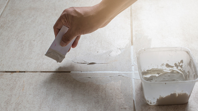 A hand filling in cracked grout lines