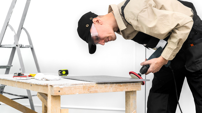 A person sanding ceramic tile on a workbench