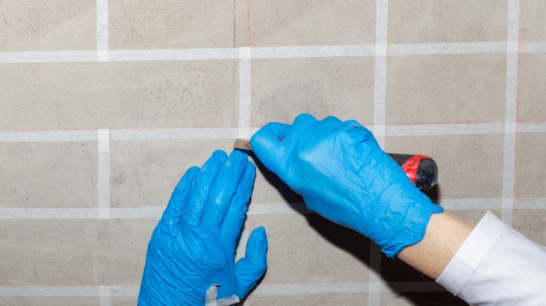 A hand wearing gloves cutting masking tape