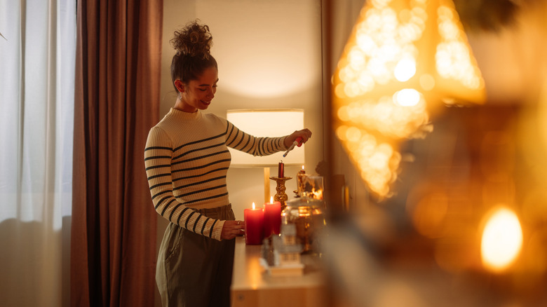 woman lights candle in warmly lit home