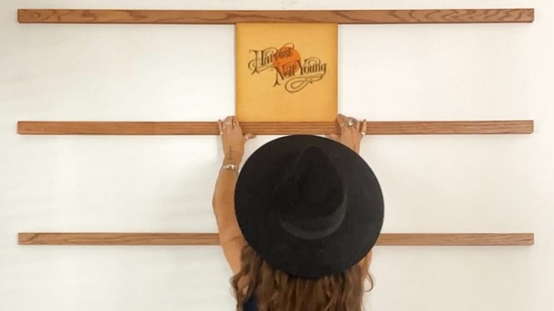 A woman arranges records on wooden slats on the wall.