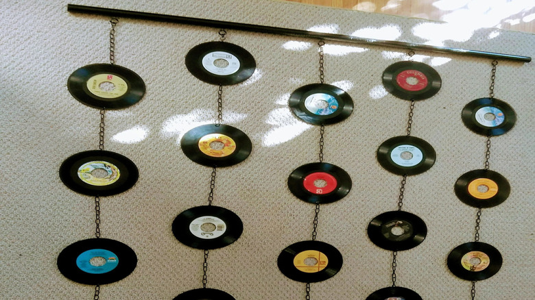 Vinyl records strung on a pole attached to a carpeted board on mounted to a wall.