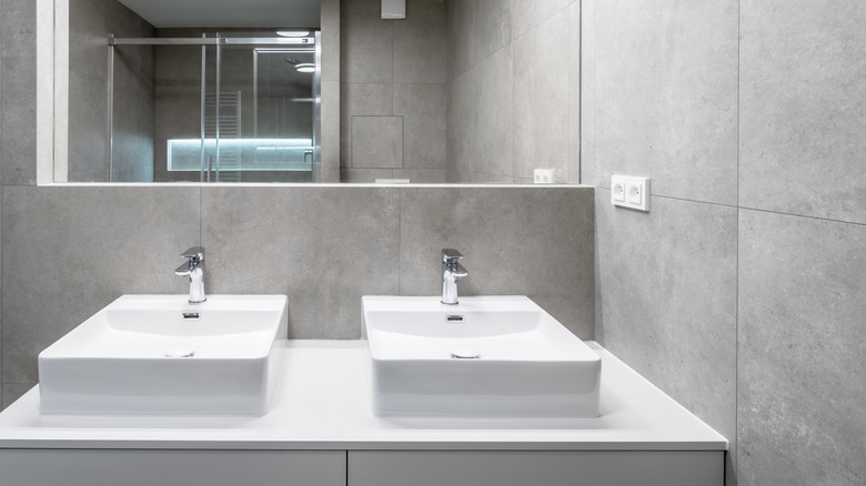 A dual bathroom vanity surrounded by polished cement tiled walls.