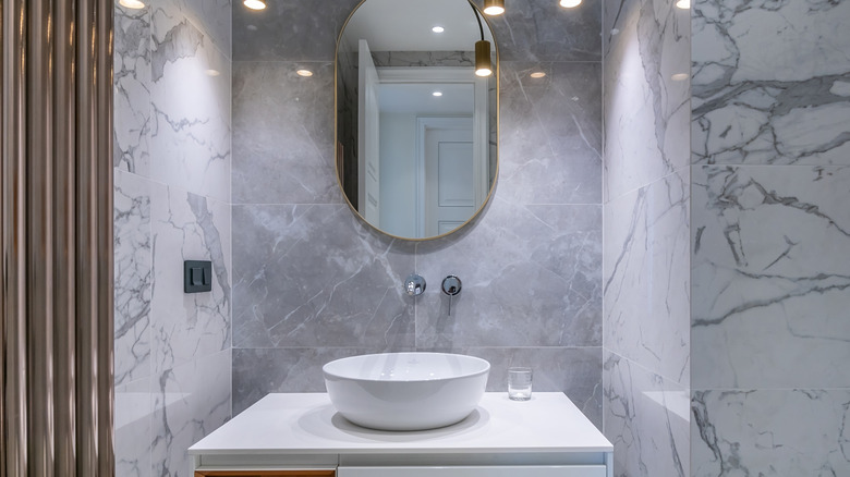 A bathroom with a white sink and marble wall tiles.