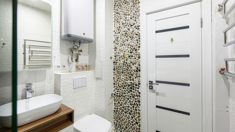 A white bathroom with a pebble tile accent wall.