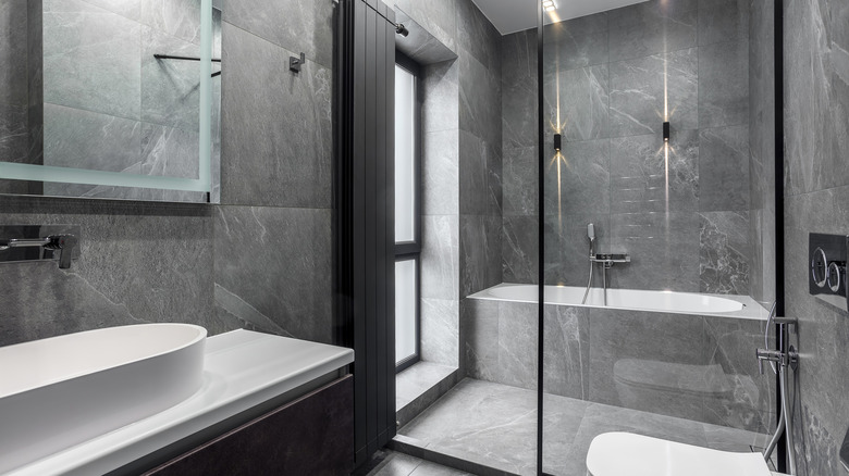 A bathroom with a wet shower and bath tub alcove covered in soapstone tile on the walls.