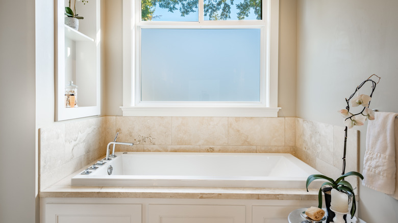 A bath tub alcove accented with travertine tile next to a window.