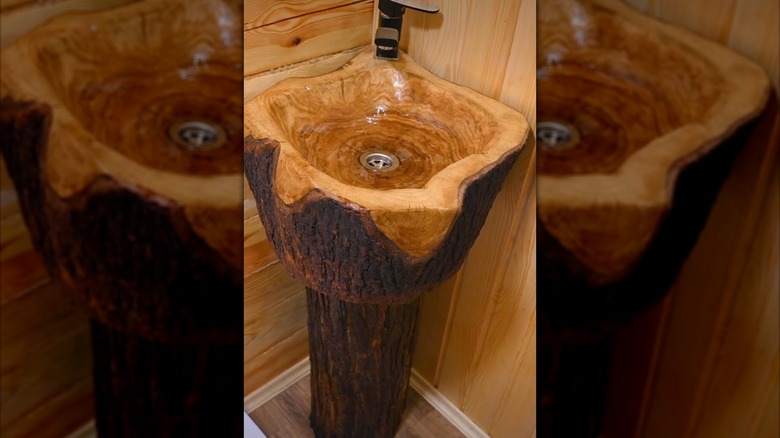 A rustic sink made from two stree stumps against a wood paneled wall in a corner