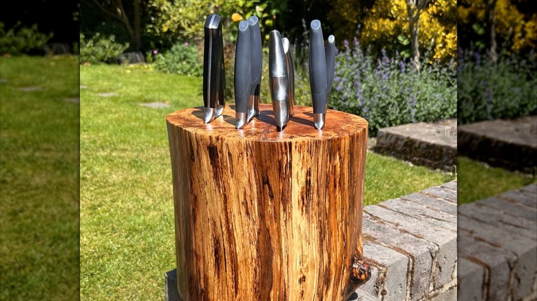 Dark wood finished knife block made from a tree stump on a brick wall outside with 8 knives in it