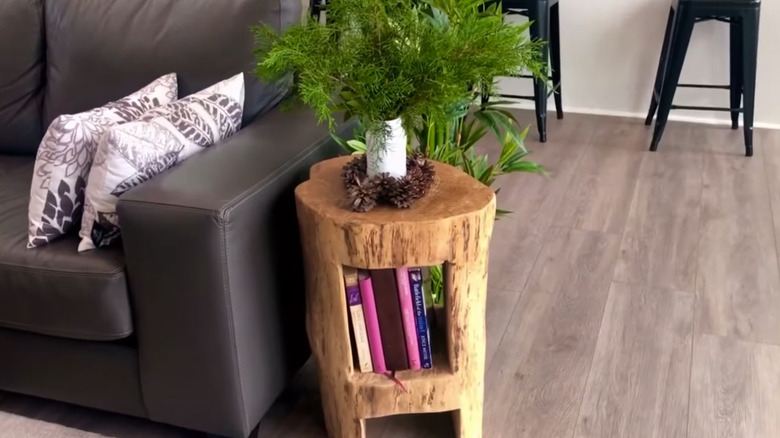 Tree stump end-table bookshelf with books and a plant on it in a living room near a couch and bar stools