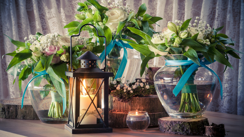 Flower vases, a lanturn, and a candle sitting on tree stump disks on a table