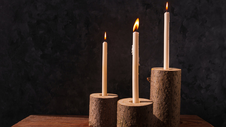 Three tall, lit candles in wood candle holders on a table in a dark room