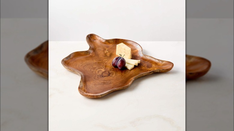 Cheese and fruit resting on top of a natural wood tray on a white stone counter