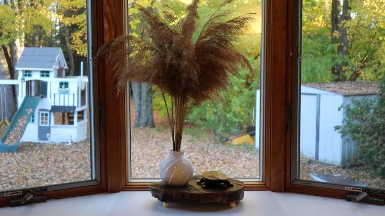 Wood shelf on a counter with a vase and decorative turtle in front of a bay window with a view of a back yard